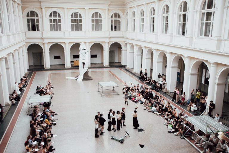 Blick von Oben ins Atrium, Performende stehen in der Mitte, darum das Publikum.