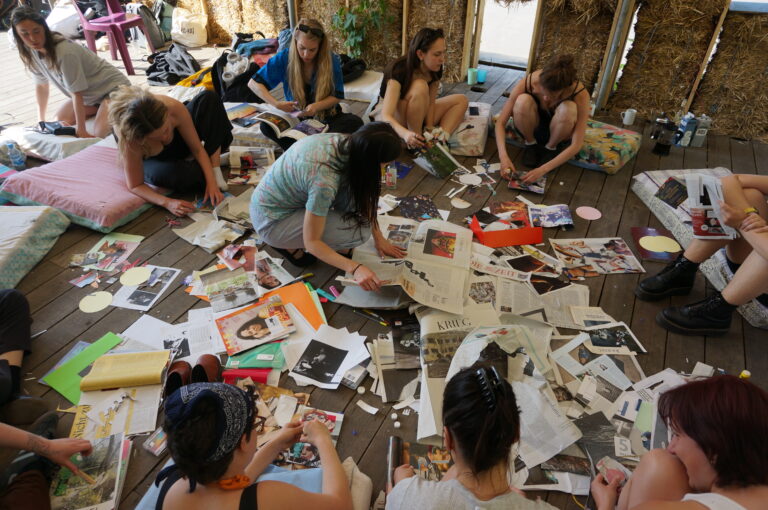 Das KHG-Team sitzt in einem Pavillion auf dem Boden und bastelt mit viel Papier eine Collage.